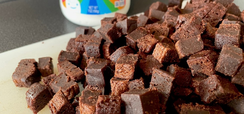 a cutting board with gooey brownie bits for ice cream chopped up and a jar of marshmallow fluff in the background